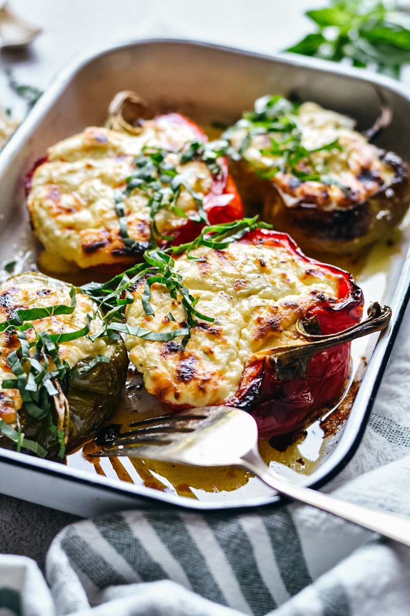 Side view of four roasted ricotta stuffed peppers in a baking dish.