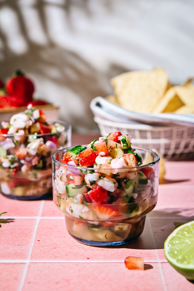 Side view of two glasses with strawberry shrimp ceviche and chips in the background.