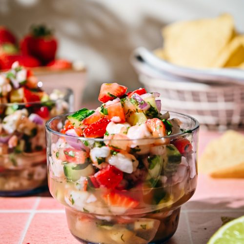 Close view of a glass of strawberry shrimp ceviche with tortilla chips in the background.