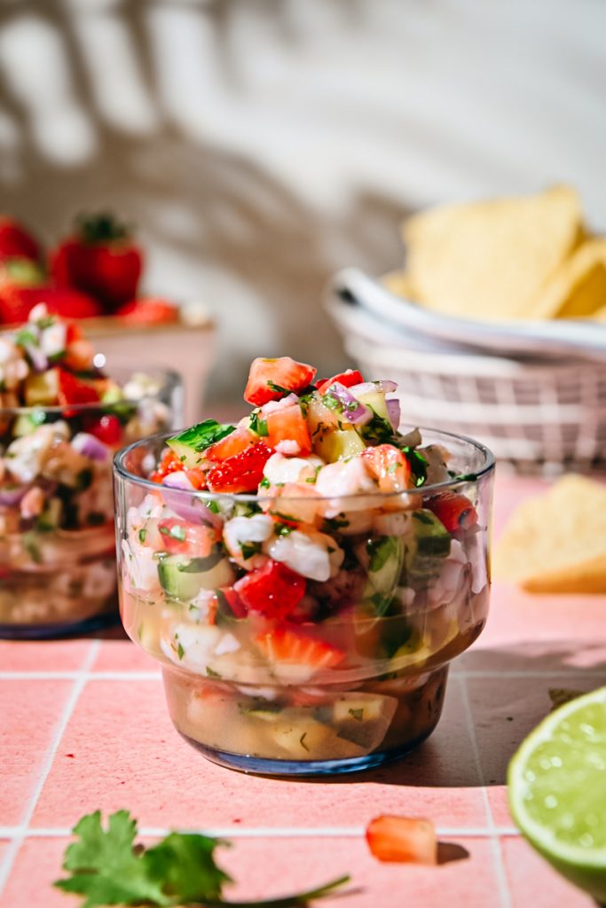 Close view of a glass of strawberry shrimp ceviche with tortilla chips in the background.