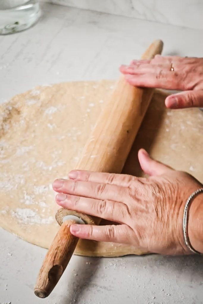 Hands using a rolling pin to roll the dough.