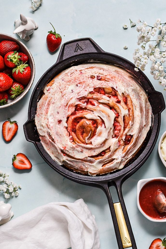 Giant strawberry roll cake in a cast iron skillet with a cream cheese glaze on top.