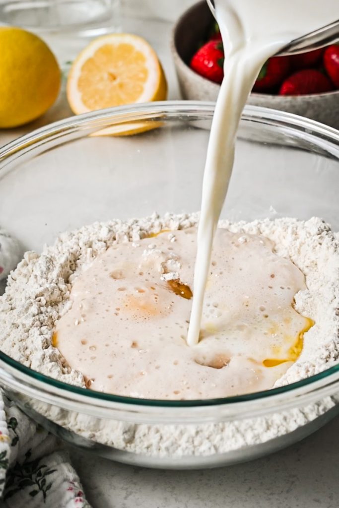 Adding milk to flour and other dough ingredients in a bowl.