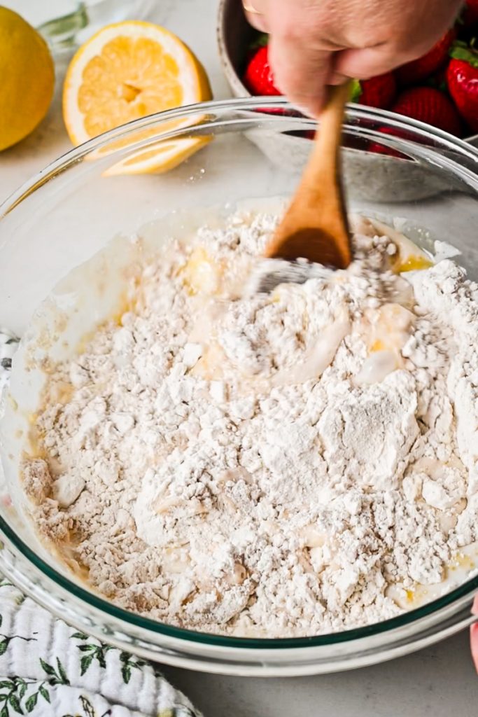 Using a wooden spoon to stir the strawberry roll dough in a bowl.