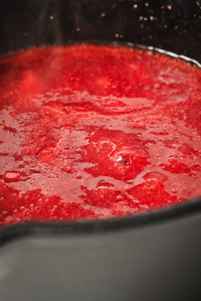 Strawberry syrup simmering in a saucepan.