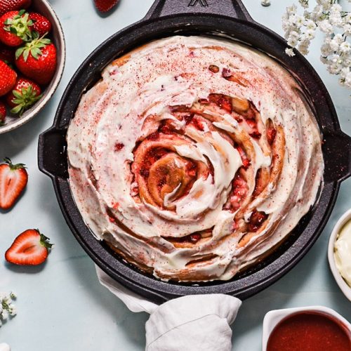 Overhead shot of giant strawberry roll cake with a cream cheese glaze on top.