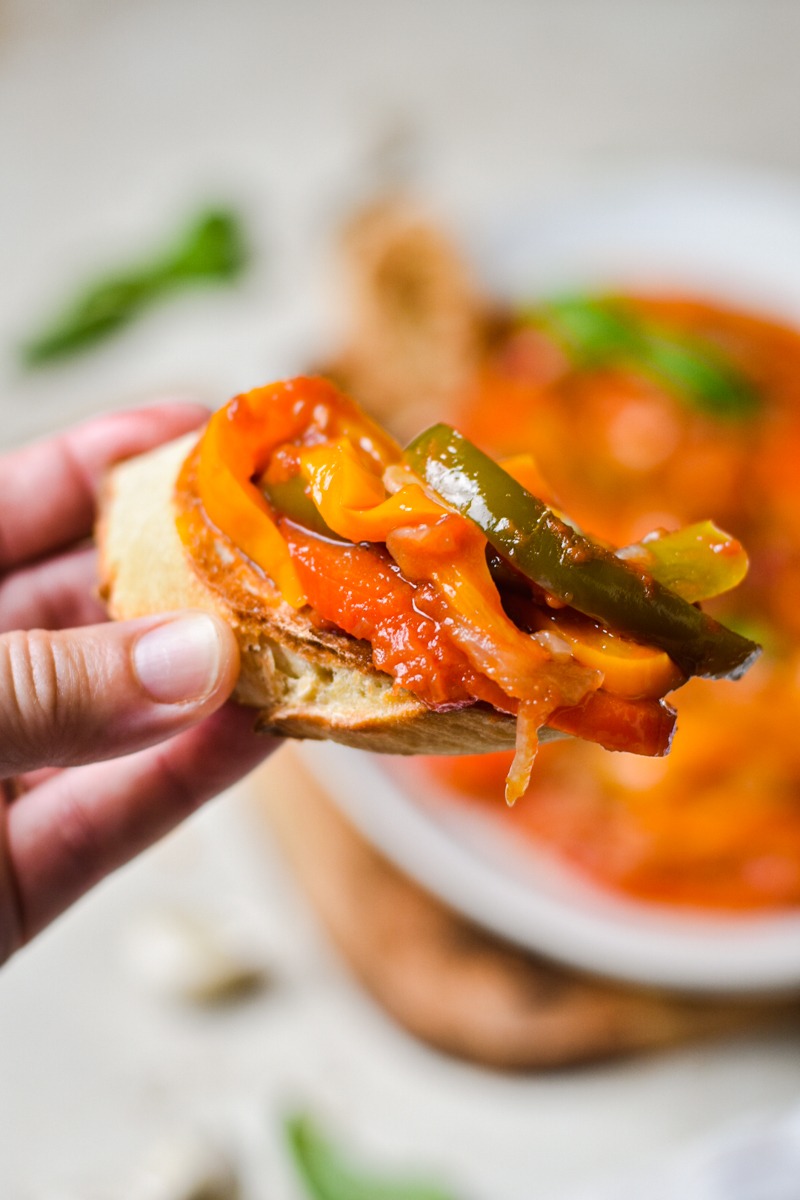 Hand holding a piece of toasted bread with peperonata on it.
