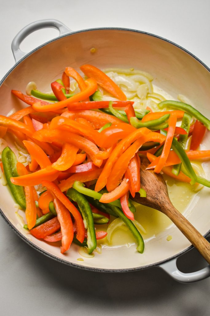Sliced bell peppers added to the onions and garlic in a skillet.