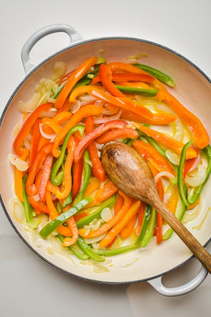 Sliced bell peppers added to the onions and garlic in a skillet.