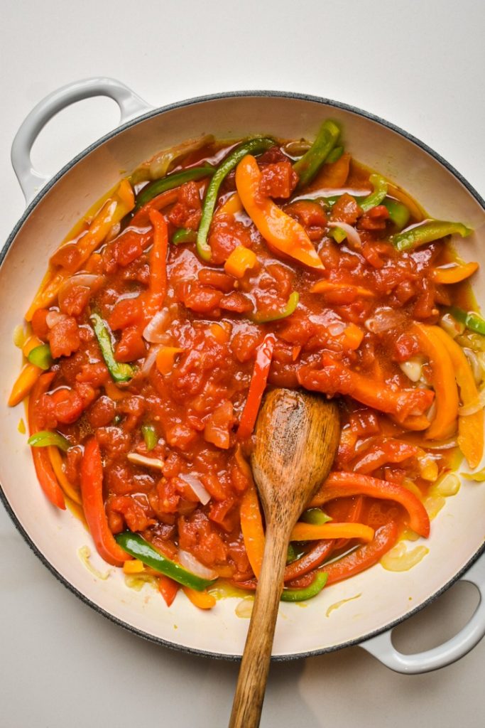Crushed tomatoes added to the pepper and onion mixture in a skillet.
