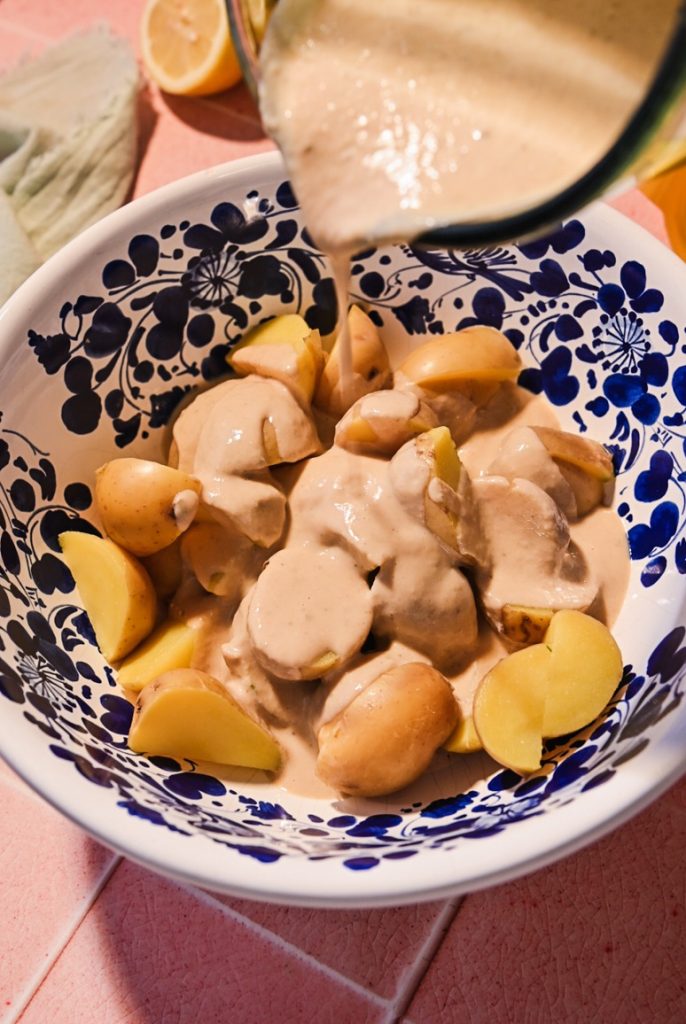 Pouring tonnato sauce over sliced boiled potatoes in a bowl.