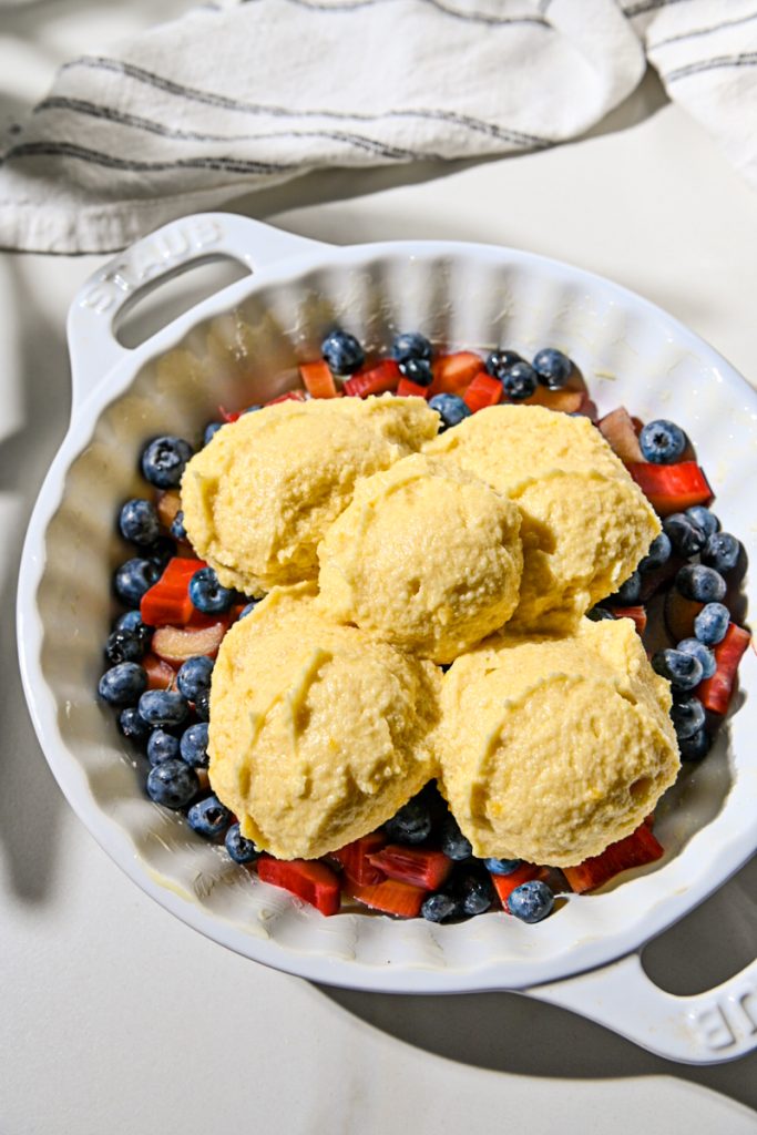 Almond cream batter scooped on top of the blueberry and rhubarb layer in a baking dish.