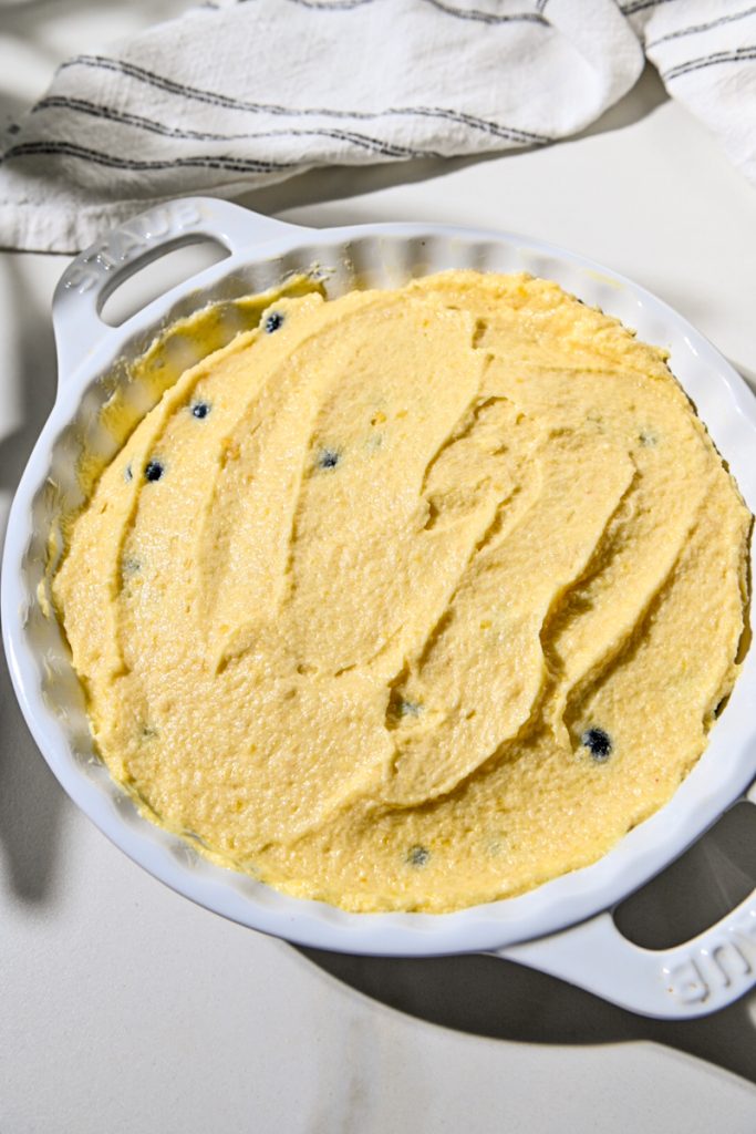 Almond cream cake batter spread over the top of the fruit in a baking dish.