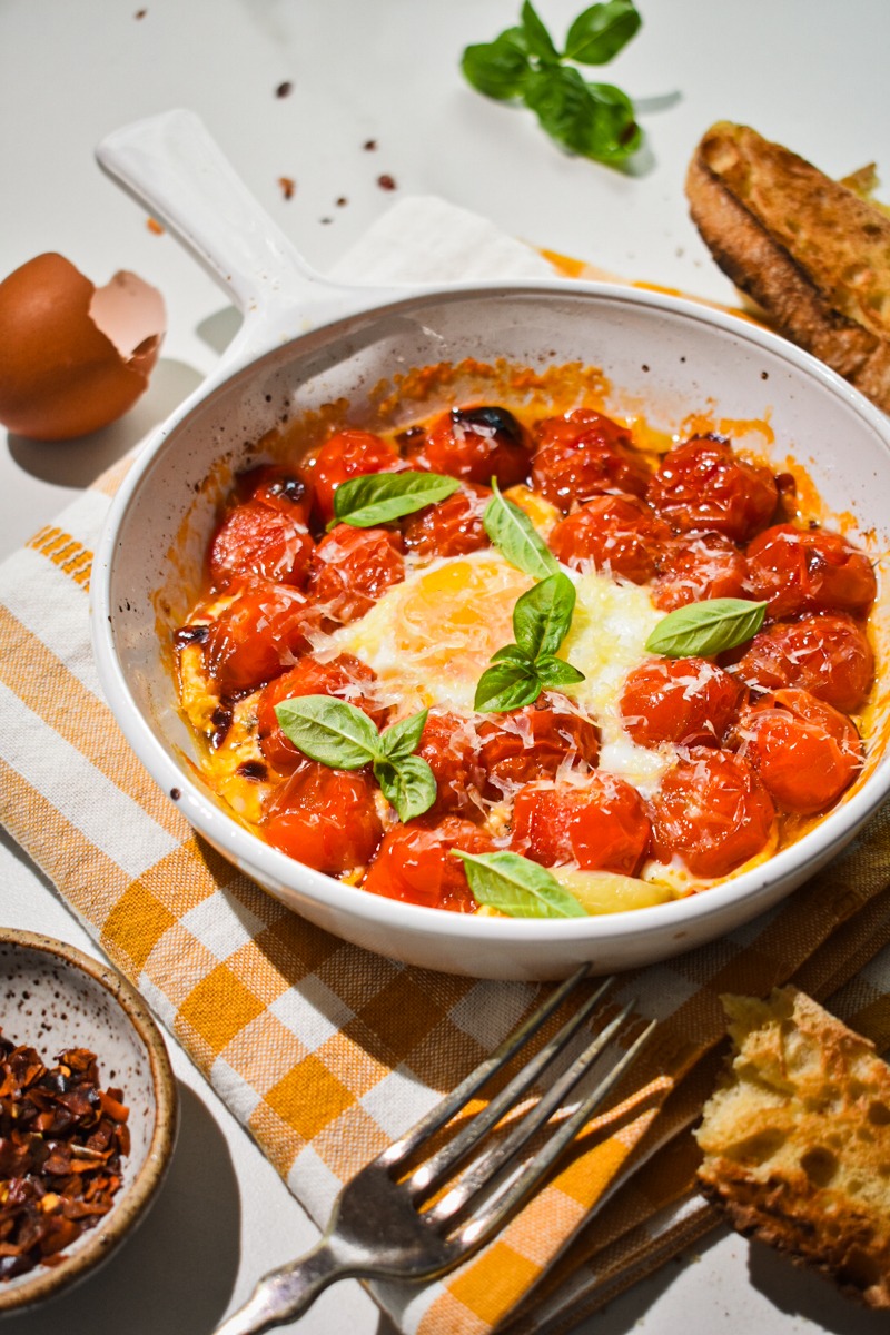 Side view of eggs in purgatory garnished with parmesan and fresh basil on top.