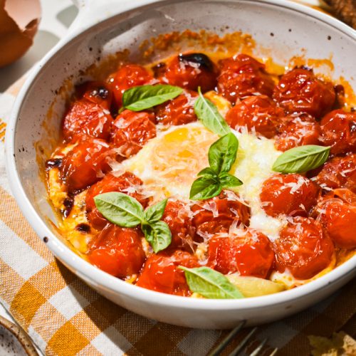 Eggs in purgatory in a white a baking dish with parm and basil on top.