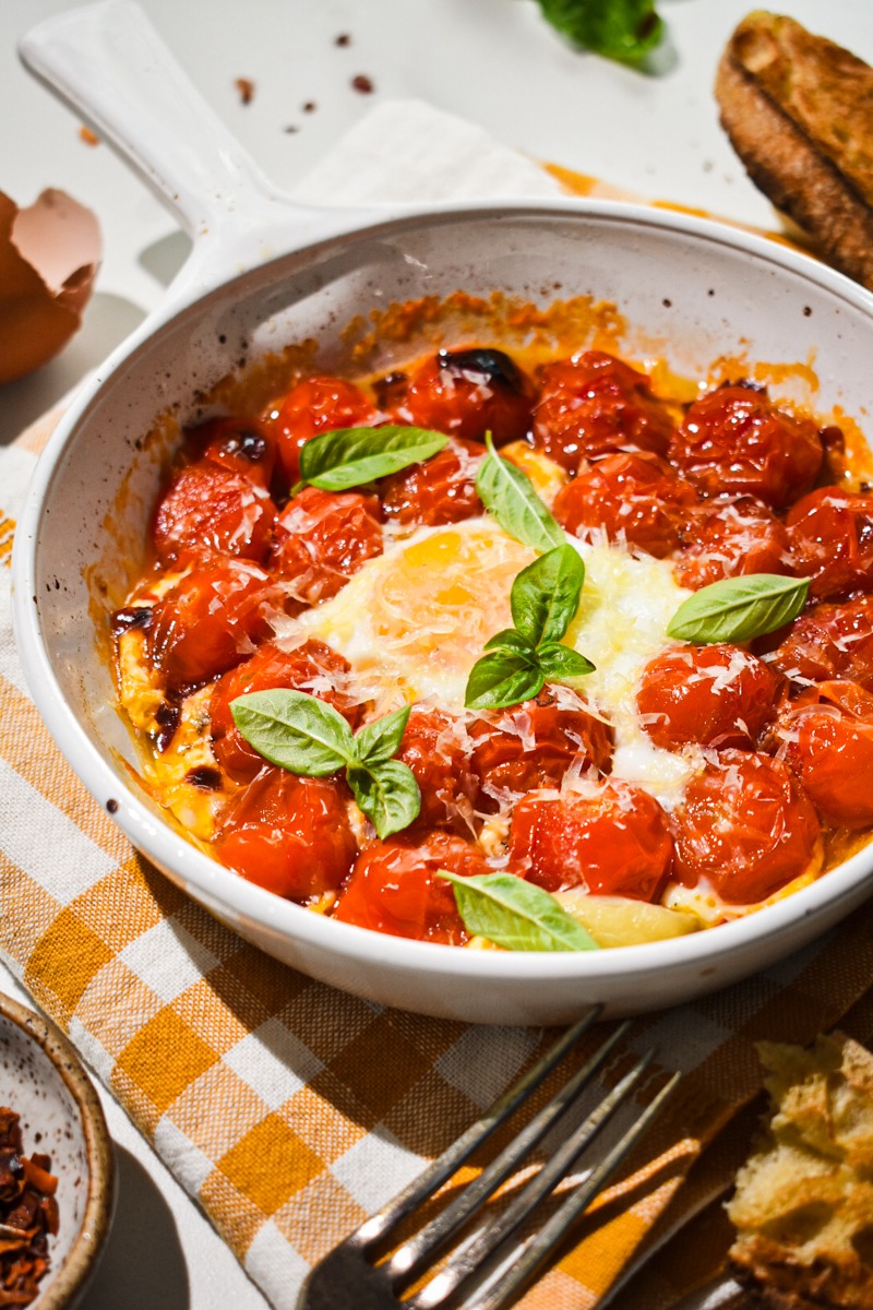 Eggs in purgatory in a white a baking dish with parm and basil on top.