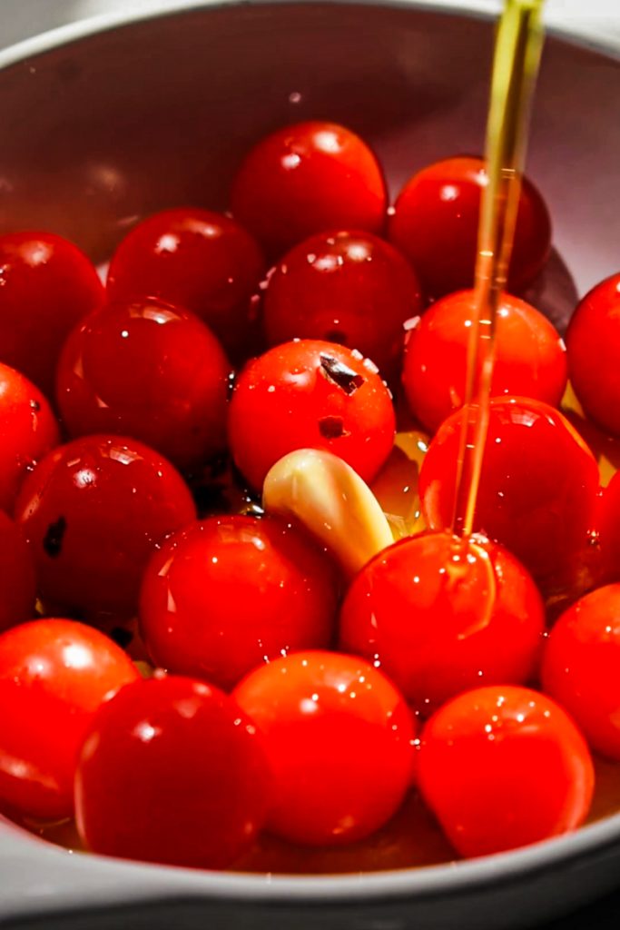 Tomatoes in a baking dish with garlic and olive oil being poured on top.