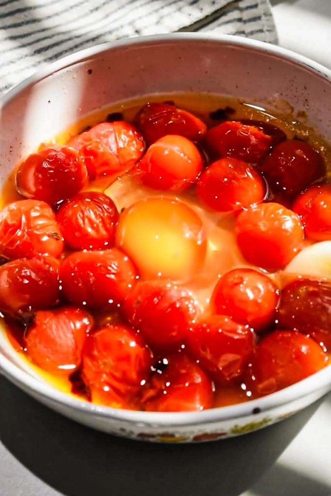 Egg cracked into the roasted tomatoes in a baking dish.