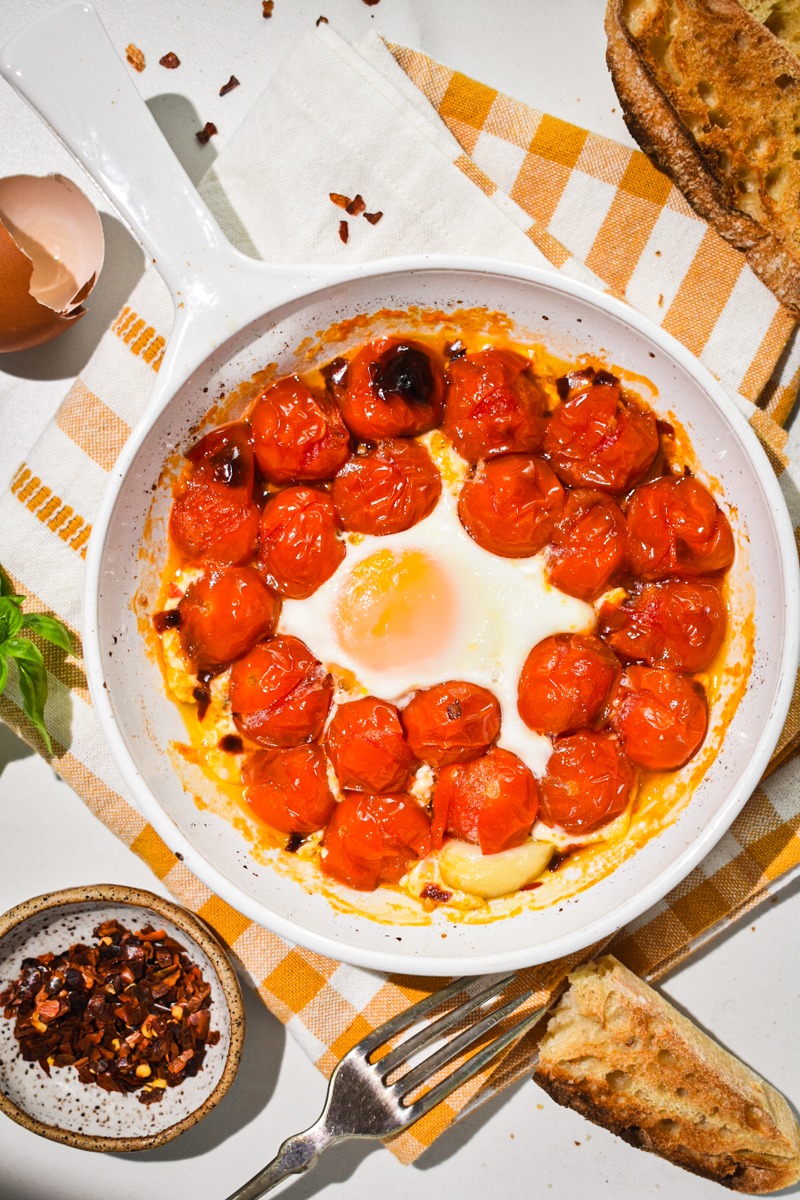 Overhead shot of eggs in purgatory with cherry tomatoes in a white baking dish.