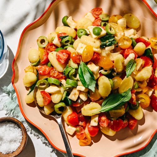 Fresh marinated tomato gnocchi salad served on an orange plate.