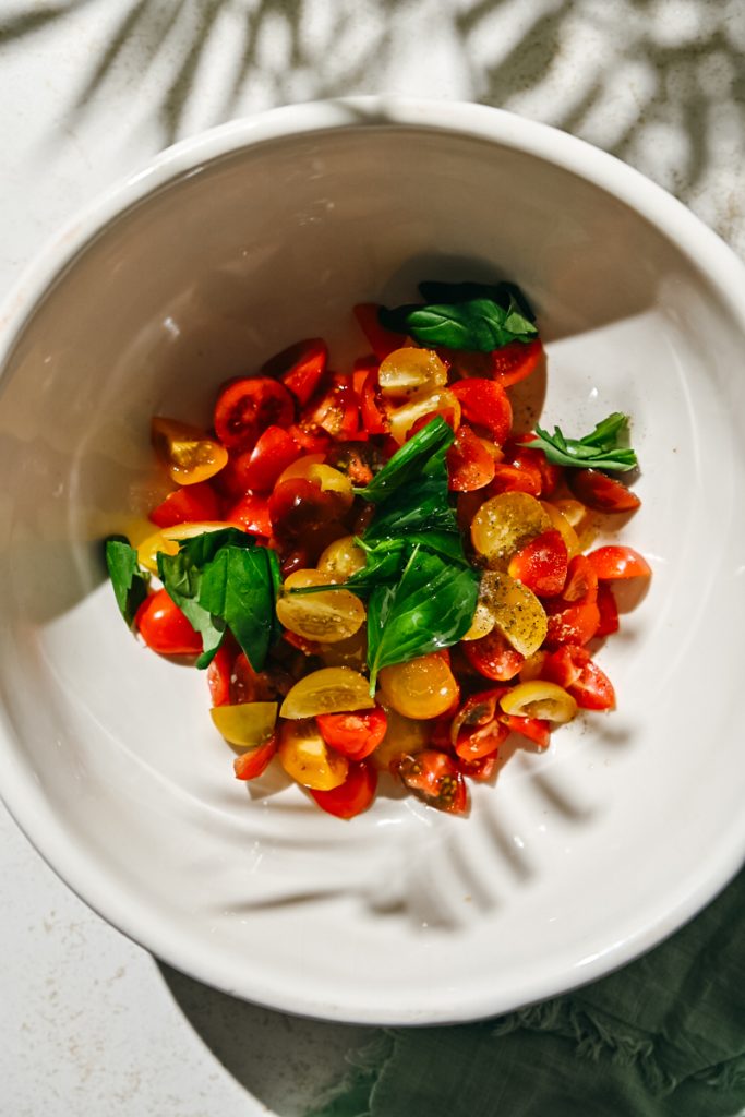 Fresh basil, olive oil, salt and pepper added to the sliced tomatoes in a bowl.