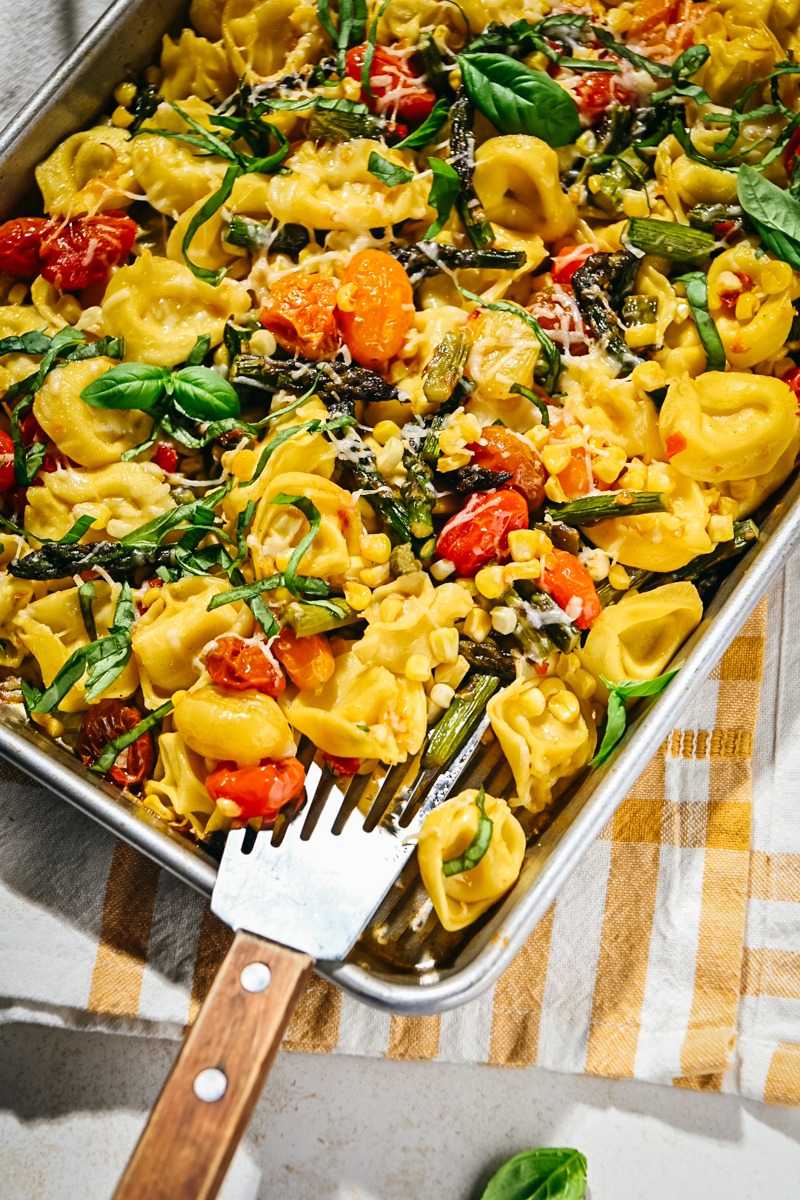 Corner of a sheet pan with summer vegetables and tortellinis.