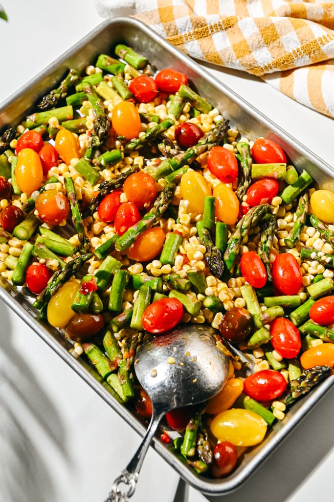 Corn, asparagus, and tomato mixture placed on a sheet pan.