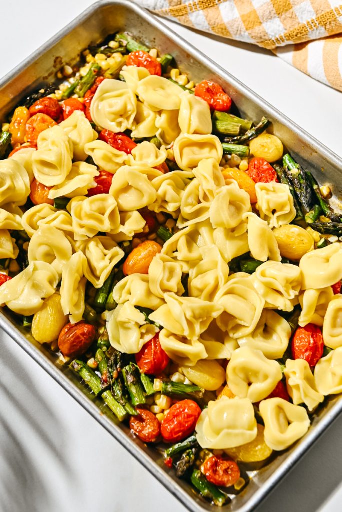 Cheese tortellini added to roasted veggies on a sheet pan.
