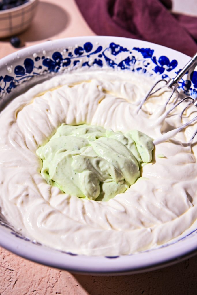 Basil ricotta mixture added to the whipped cream in a bowl.