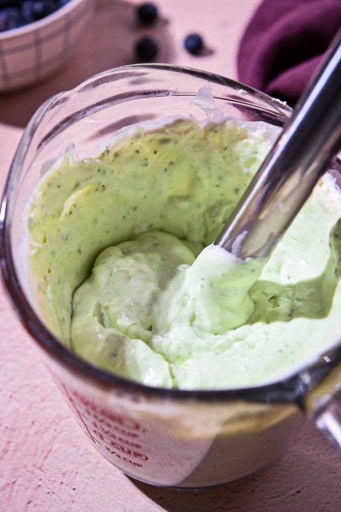 Basil, heavy cream and ricotta being blended by an immersion blender.