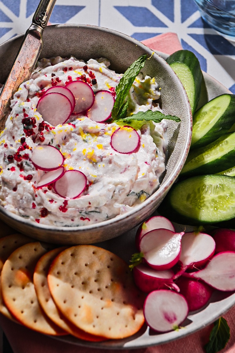 Ricotta radish dip served in a bowl on a plate with veggies and crackers.
