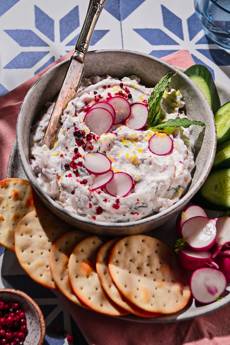 Close up of ricotta radish dip served in a bowl on a plate with crackers and veggies.