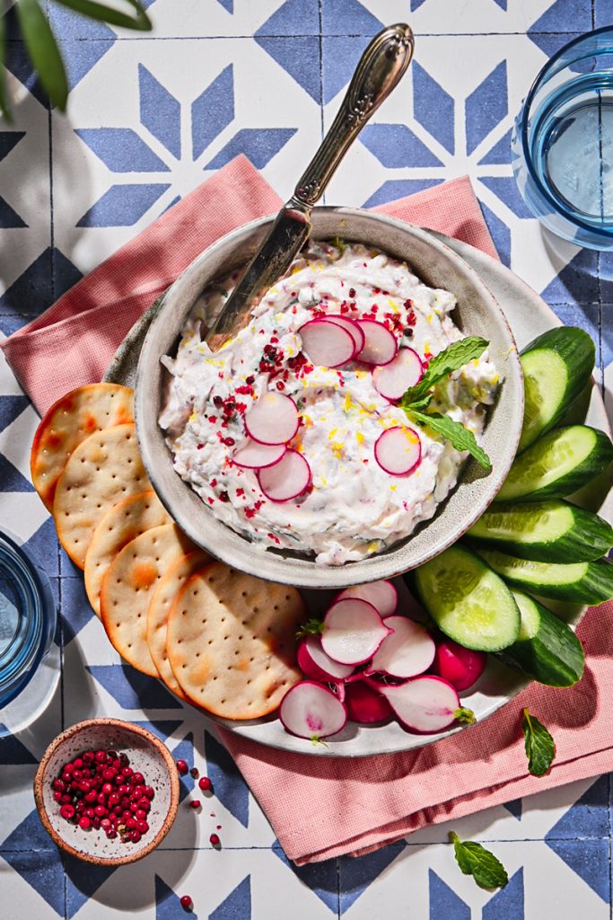 Overhead shot of ricotta radish dip in a bowl with crackers and veggies on a plate.