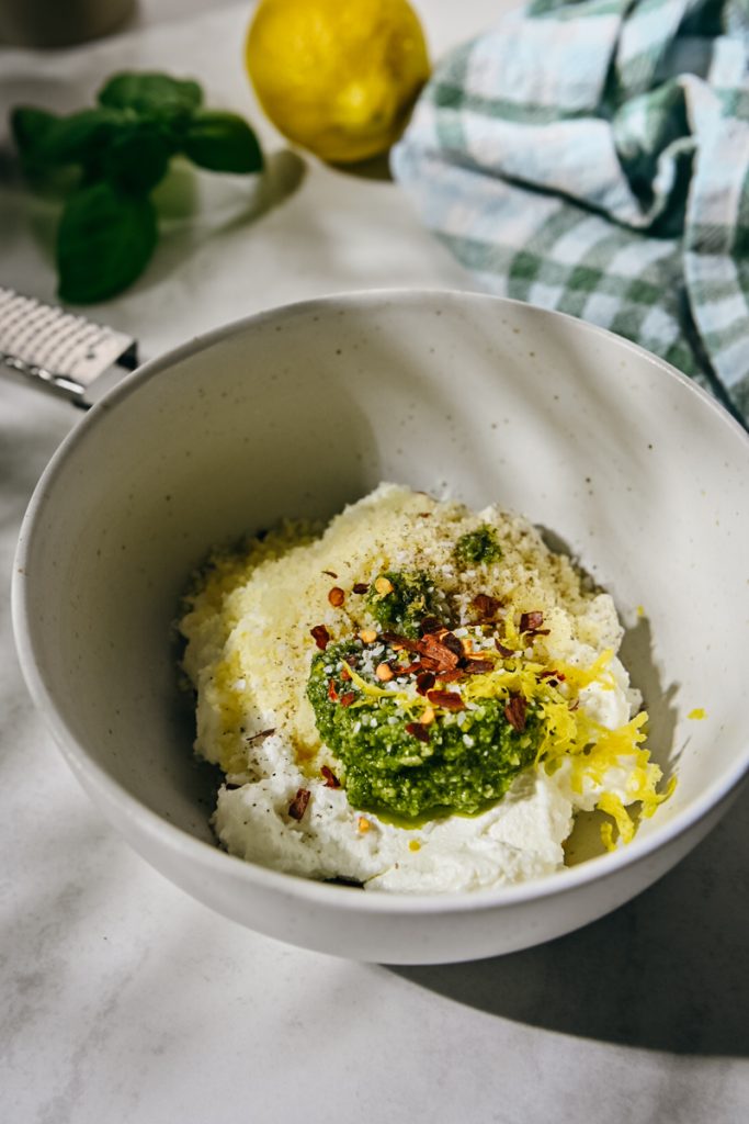 Ricotta, parmesan cheese, pesto, lemon zest and red pepper flakes in a bowl.