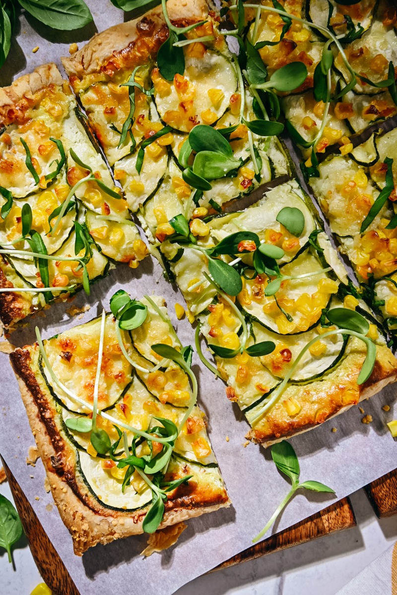 Overhead shot of zucchini tart with corn and microgreens on top.