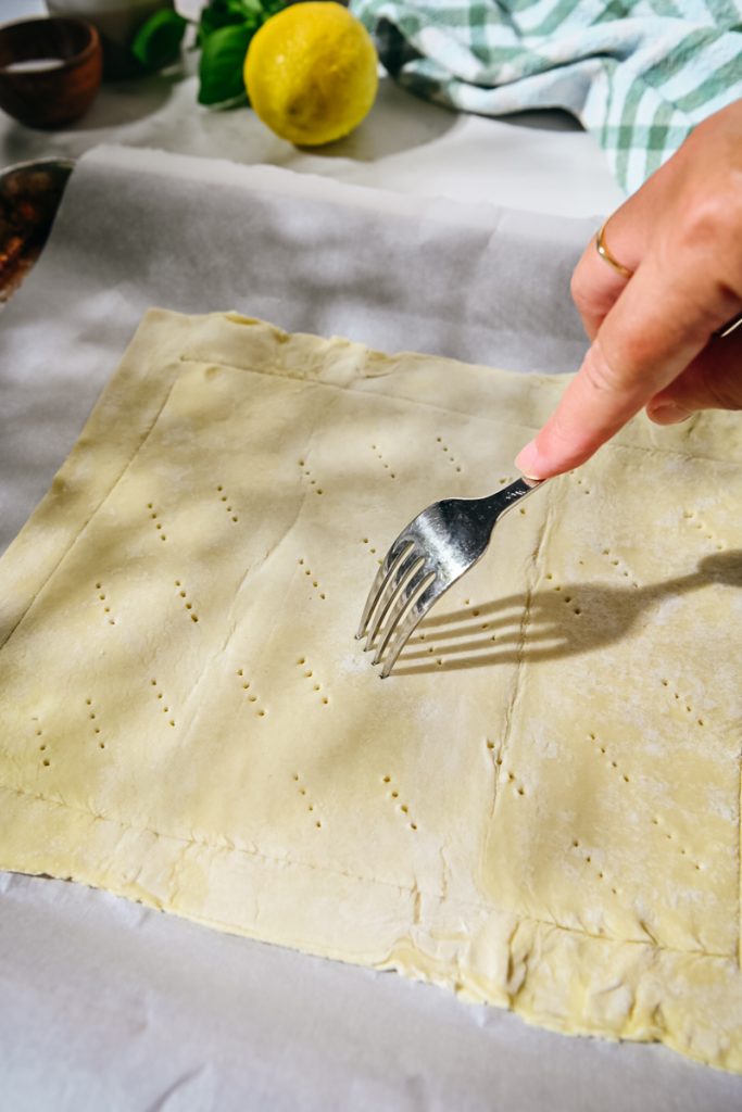 Using a fork to poke holes into a sheet of puff pastry.