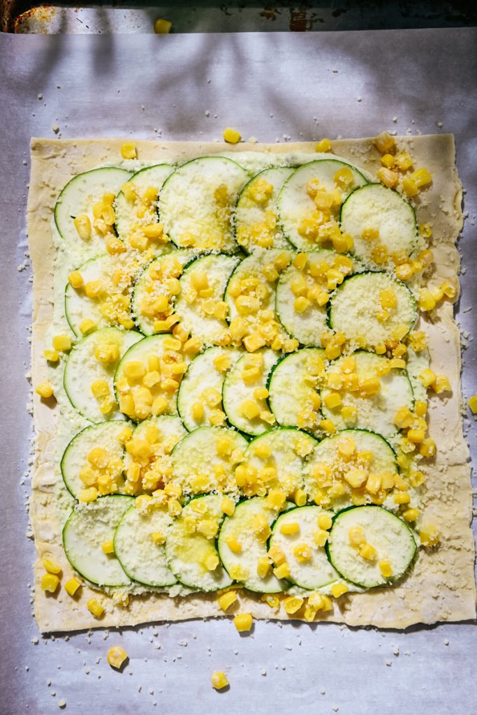 Corn and parmesan on top of the zucchini layer on a tart.