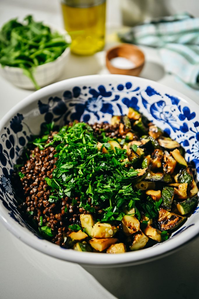 Lentils, herbs, and zucchini added to a bowl with pasta.