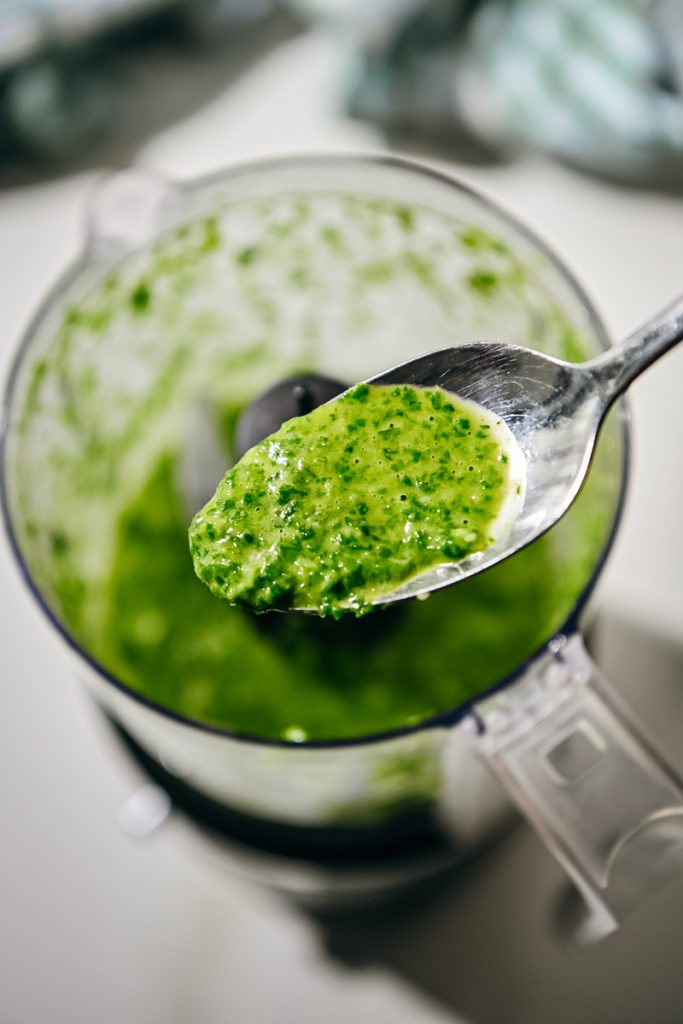 Spoonful of arugula vinaigrette in a food processor.