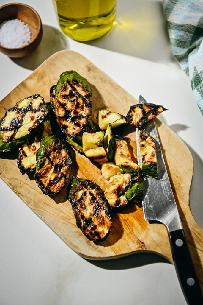 Chopping sliced grilled zucchini on a cutting board.