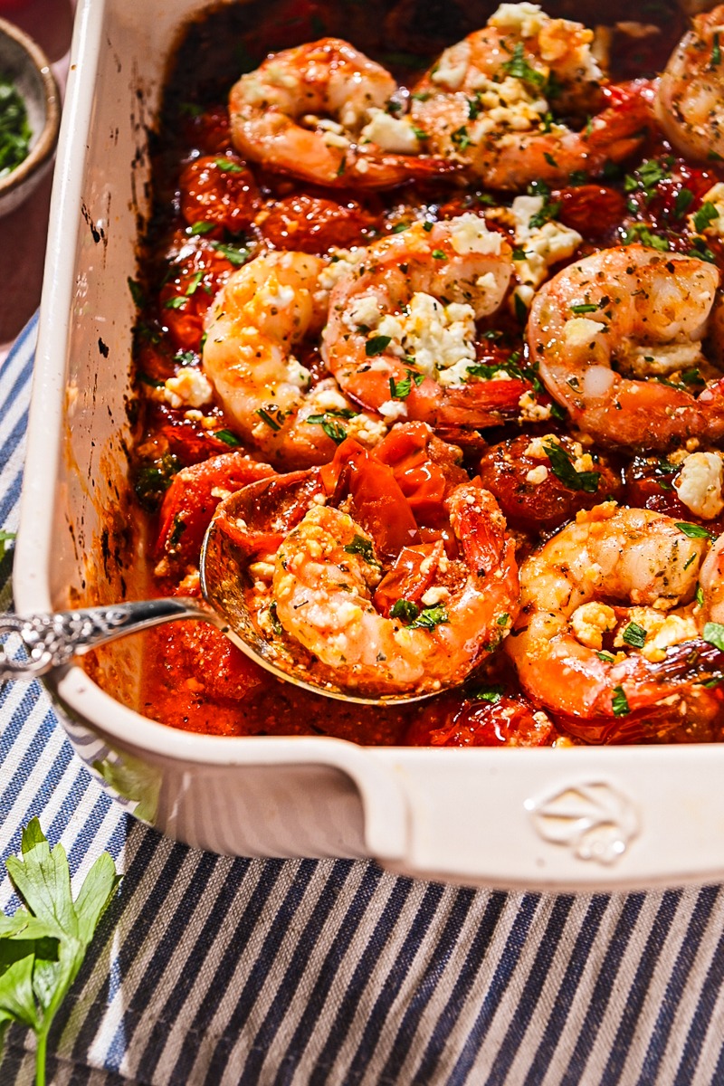 Spoon scooping up a shrimp from the shrimp saganaki in a baking dish.