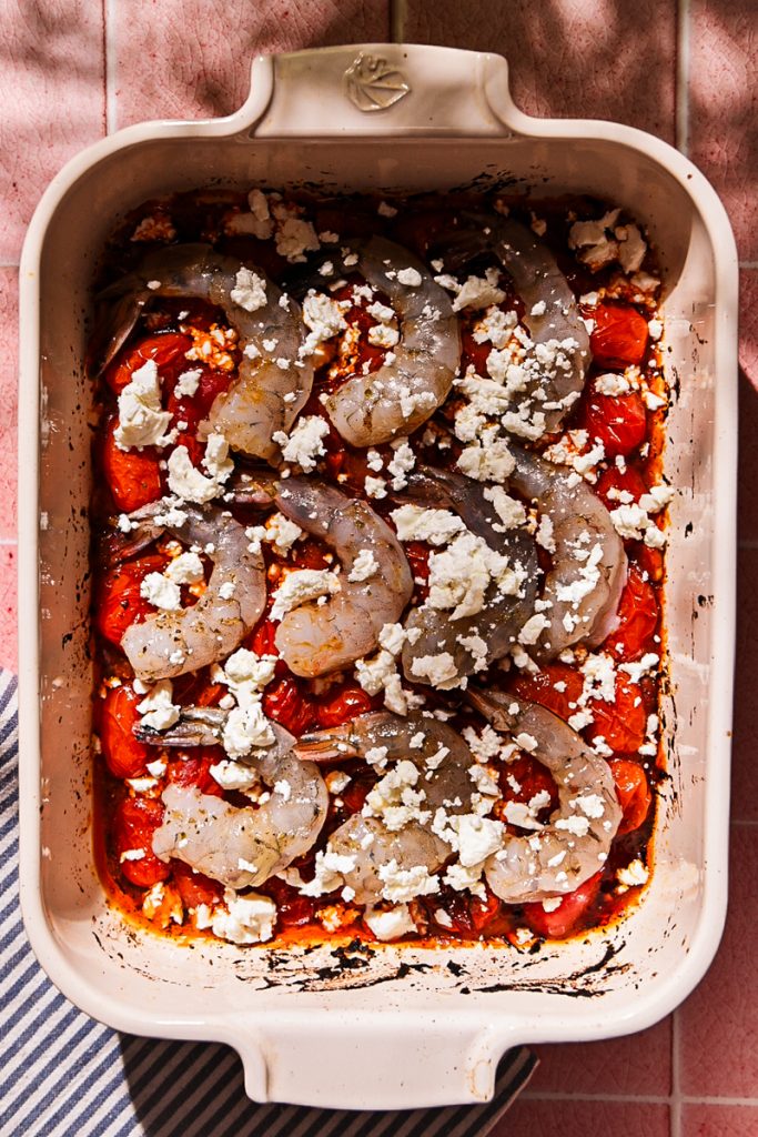 Feta crumbled on top of the shrimp in roasted tomatoes in a baking dish.