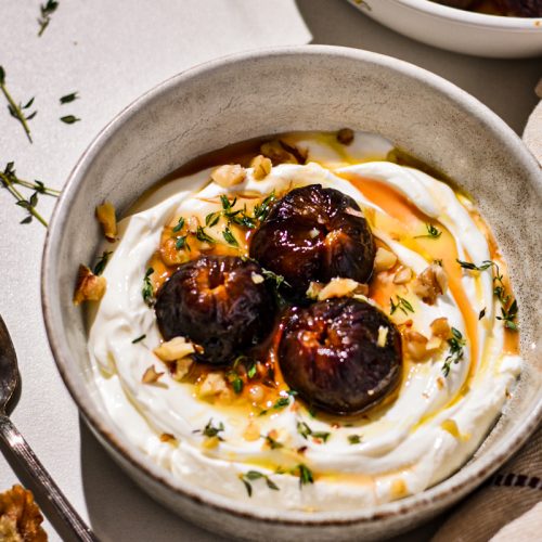 Roasted figs with yogurt in a bowl topped with walnuts and thyme.