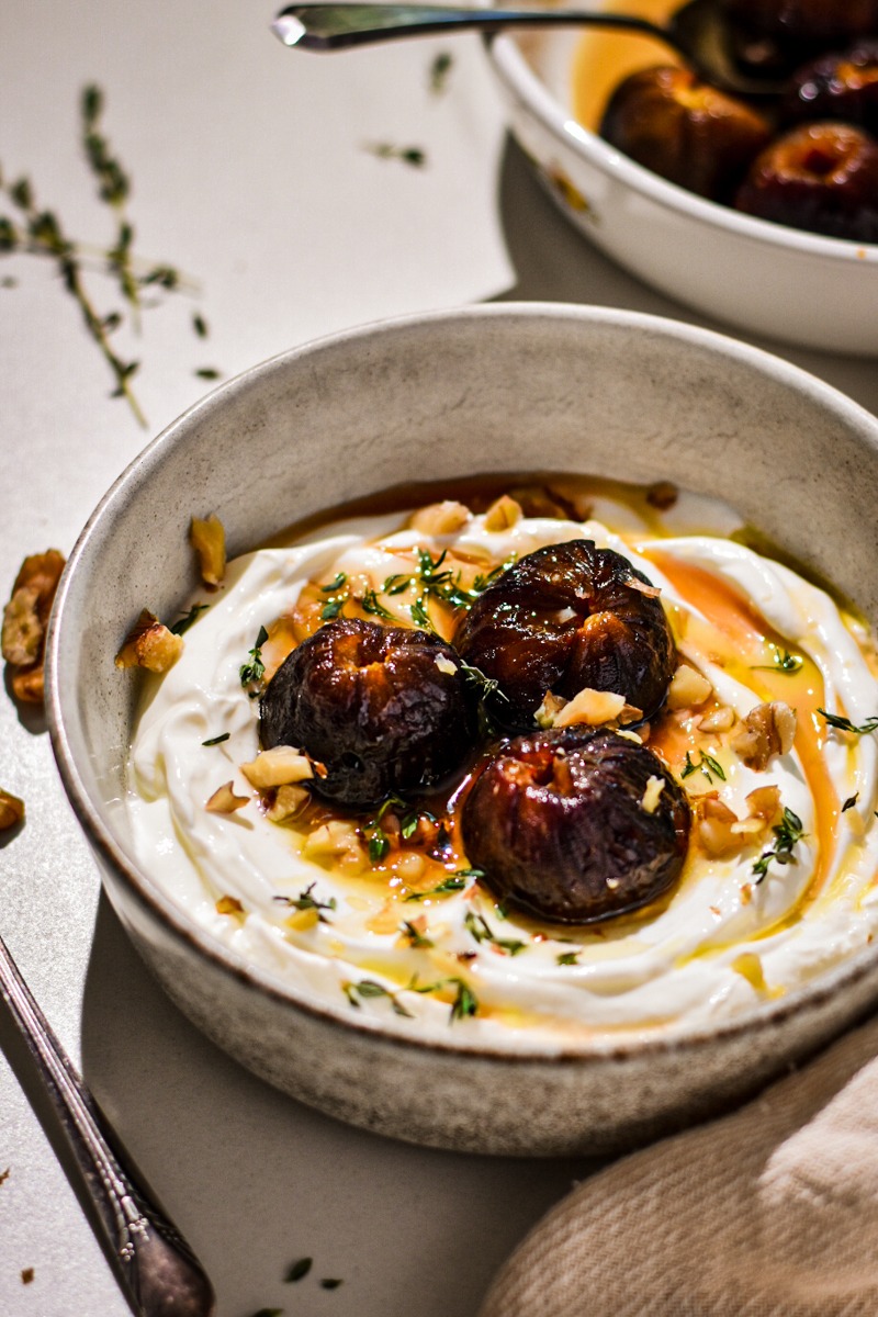 Bowl of roasted figs with yogurt garnished with walnuts and thyme.