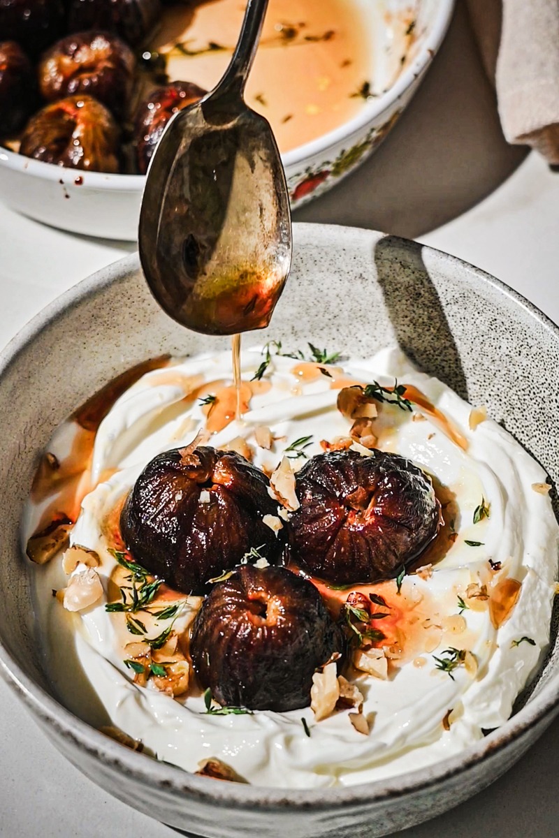 Roasted figs on top of yogurt in a bowl drizzling the fig juices on top.
