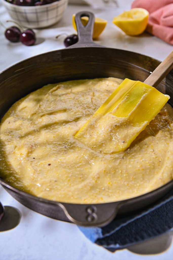 Spreading cherry spoon cake batter into a cast iron skillet.