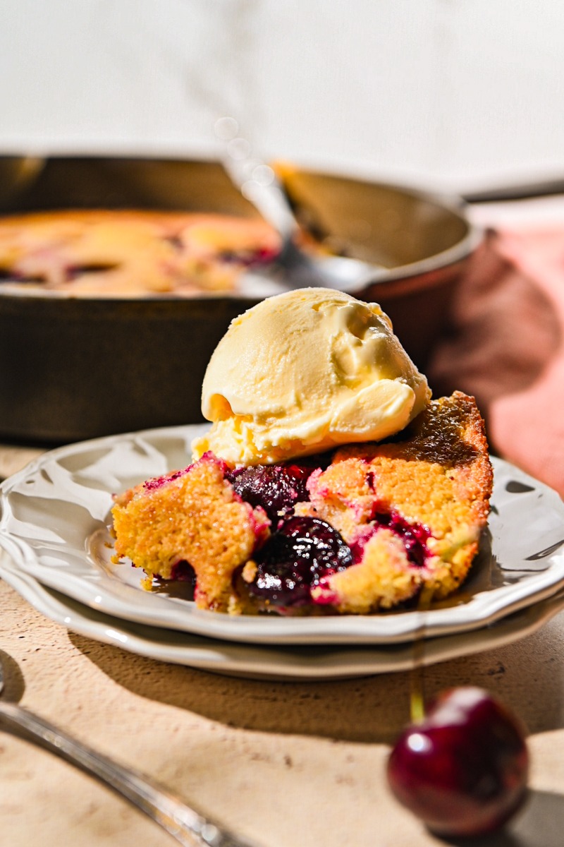 Side view of a portion of cherry spoon cake on a plate topped with ice cream.