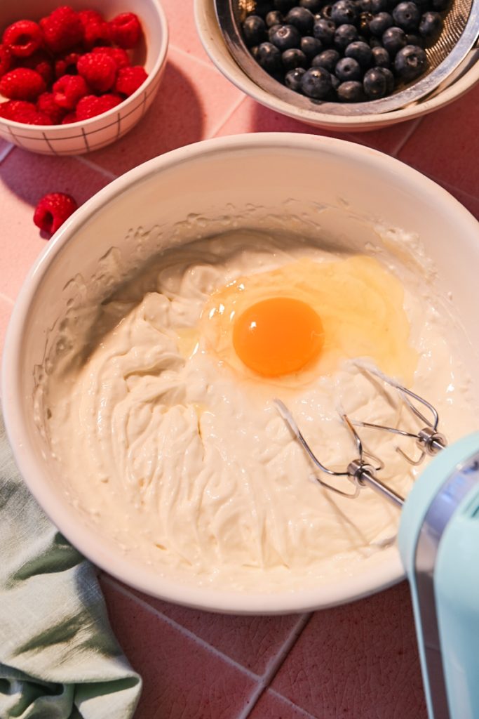 Adding egg in the cream cheese mixture in a bowl.
