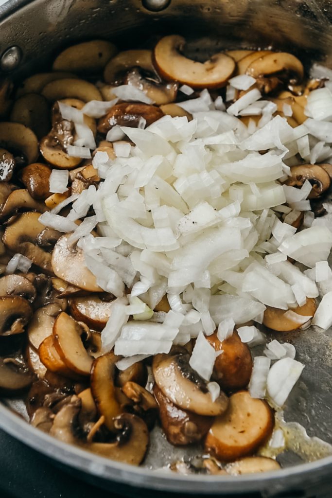 Onions added to the mushrooms in a skillet.