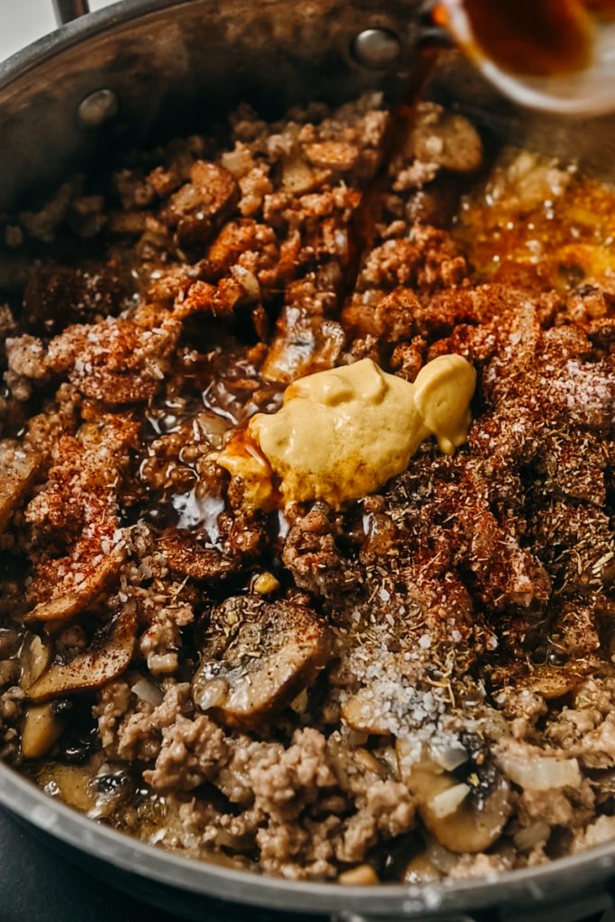 Spices and dijon mustard added to the ground veal mixture in a skillet.